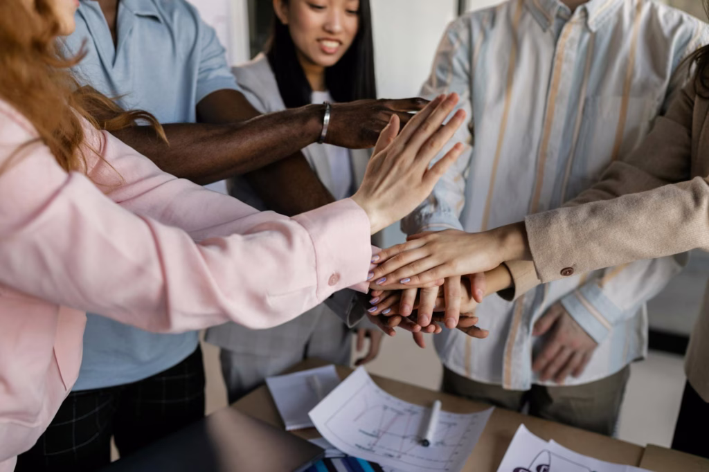 Diverse team members putting hands together in an office, symbolizing collaboration and unity.