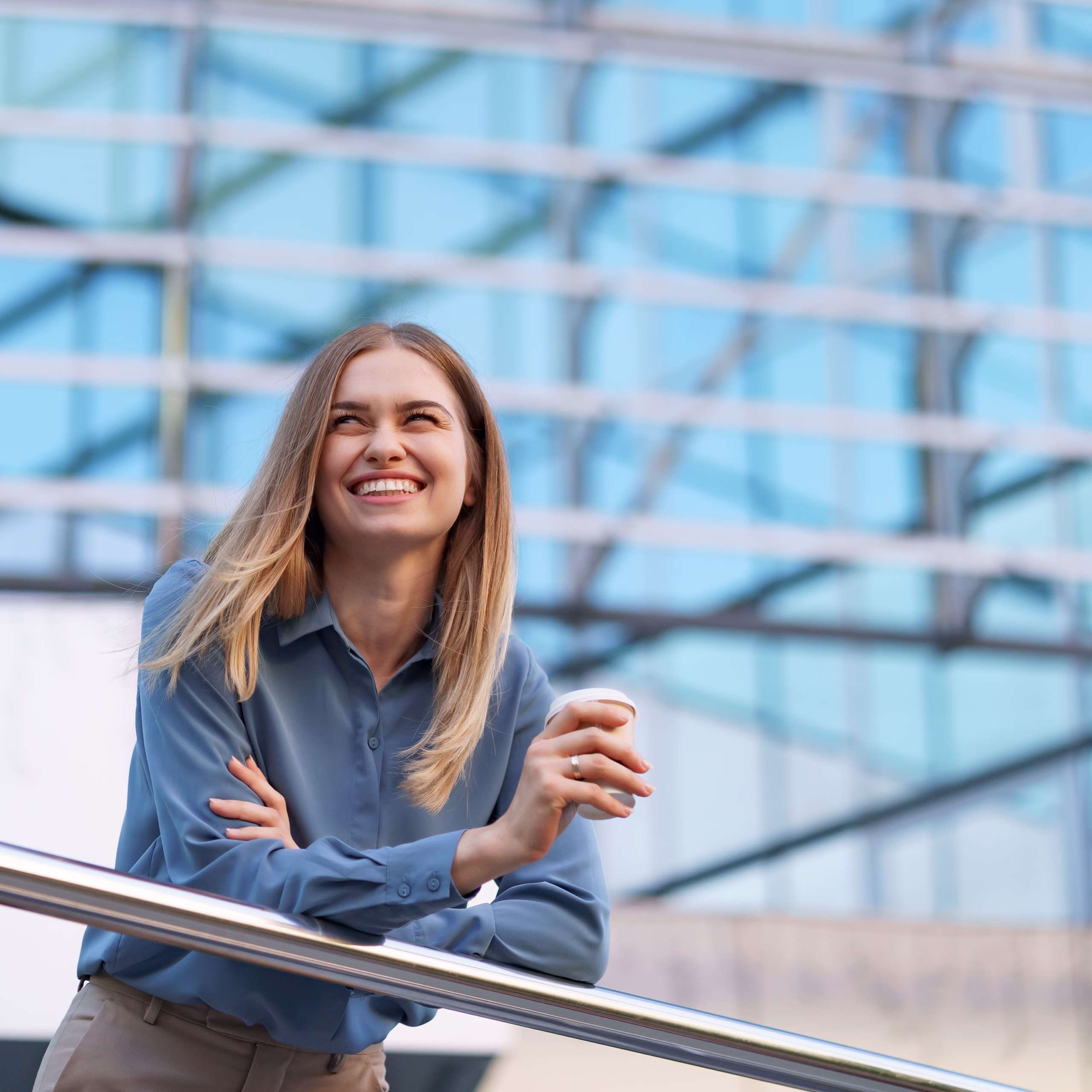 Young smiling professional woman having a coffee break during her full working day. She holds a paper cup outdoors near the business building while relaxing and enjoying her beverage.